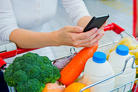 Woman with phone in her hand with vegetables and milk in her cart
